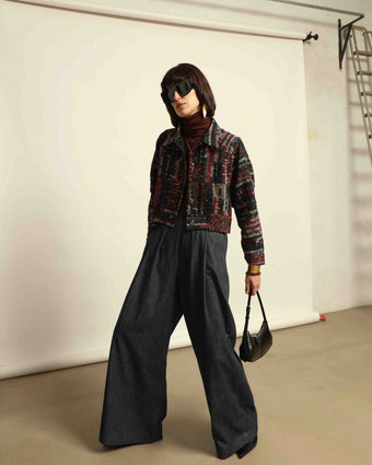 Model is wearing the Denim Parigi Wide-Leg Trousers by House of Nomad Stories, featuring a rich dark denim finish, mid-rise elasticated waist, front pleats, and a relaxed wide-leg silhouette.
