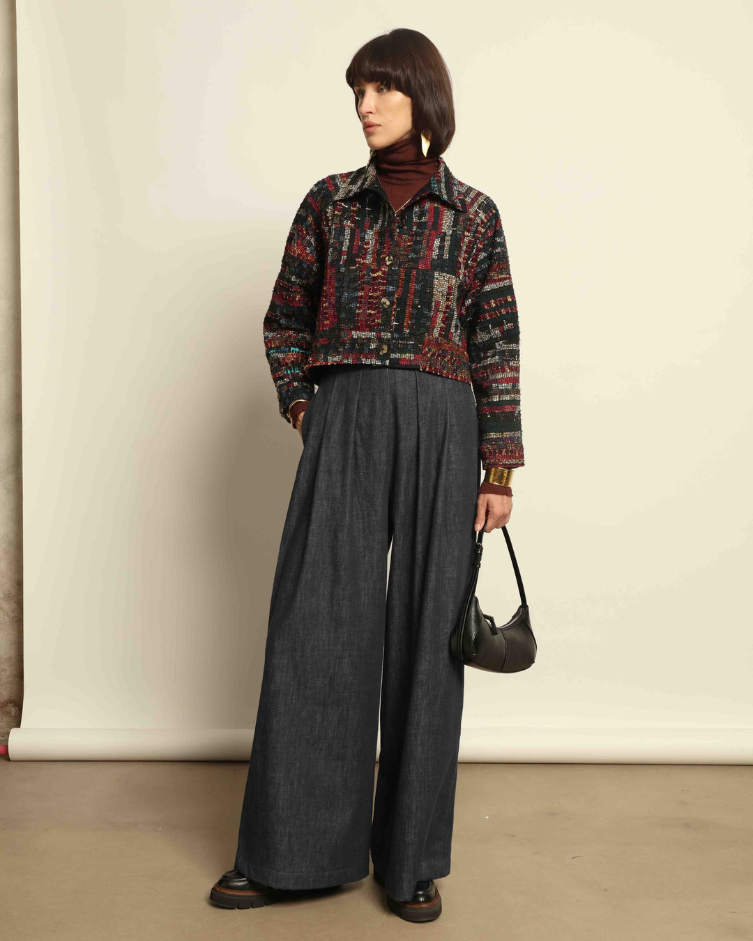 Model is wearing the Denim Parigi Wide-Leg Trousers by House of Nomad Stories, featuring a rich dark denim finish, mid-rise elasticated waist, front pleats, and a relaxed wide-leg silhouette.
