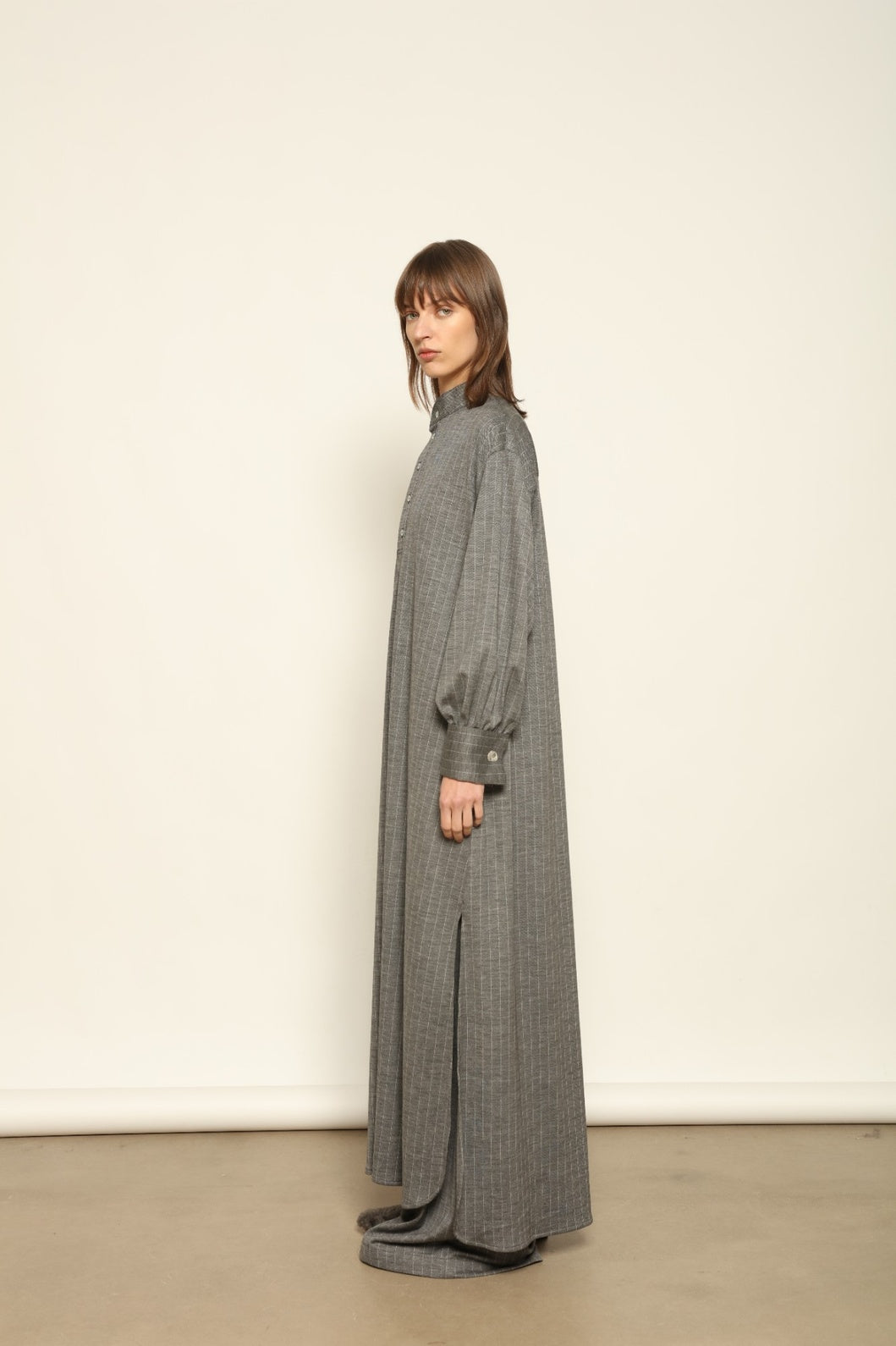 Model is wearing the Paul Dress by House of Nomad Stories, made from sustainable wool with vertical stripes, a stand collar, and versatile styling for effortless elegance.