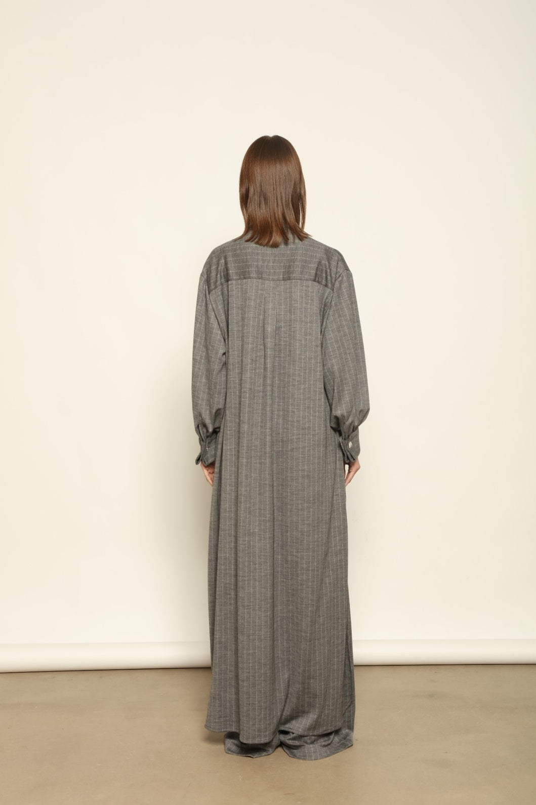 Model is wearing the Paul Dress by House of Nomad Stories, made from sustainable wool with vertical stripes, a stand collar, and versatile styling for effortless elegance.