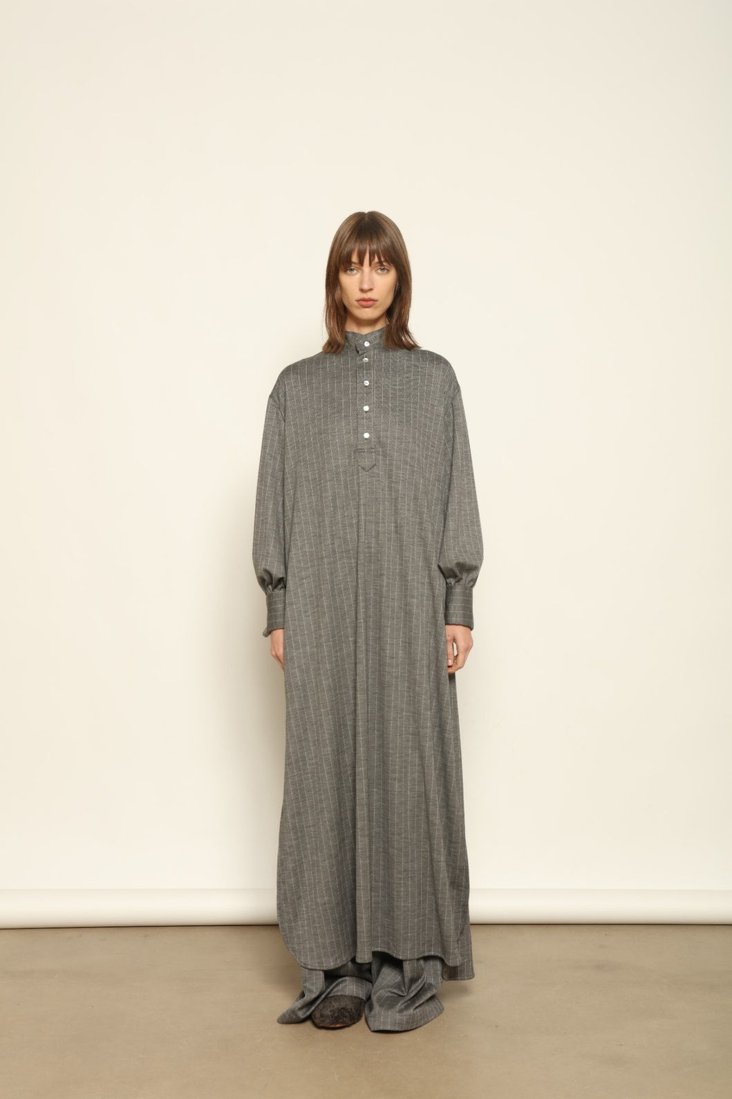 Model is wearing the Paul Dress by House of Nomad Stories, made from sustainable wool with vertical stripes, a stand collar, and versatile styling for effortless elegance.