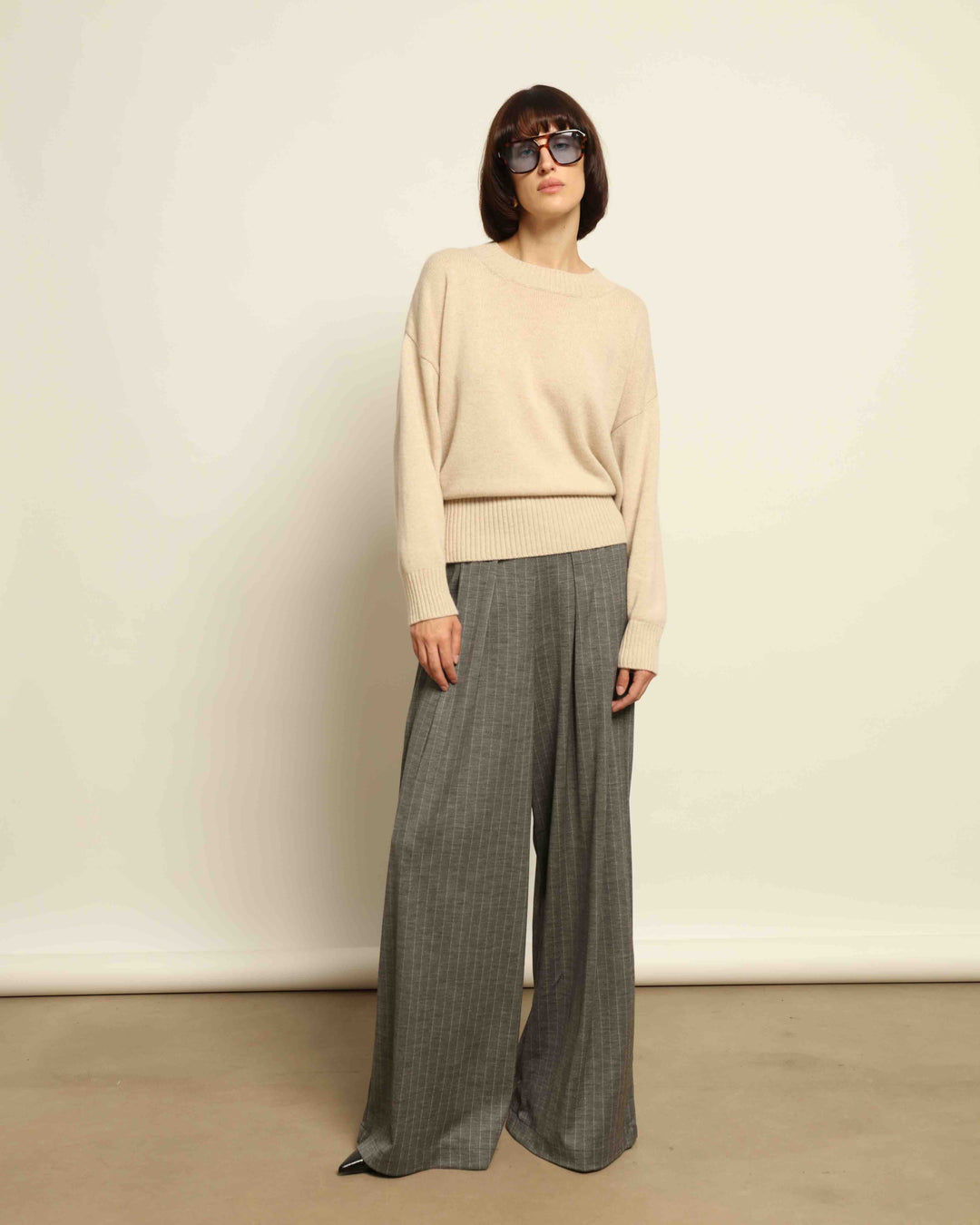 Model is wearing the Grey Parigi Pinstriped Jersey Trousers by House of Nomad Stories, featuring a tailored silhouette, refined grey pinstripes, and an elegant straight-leg fit.