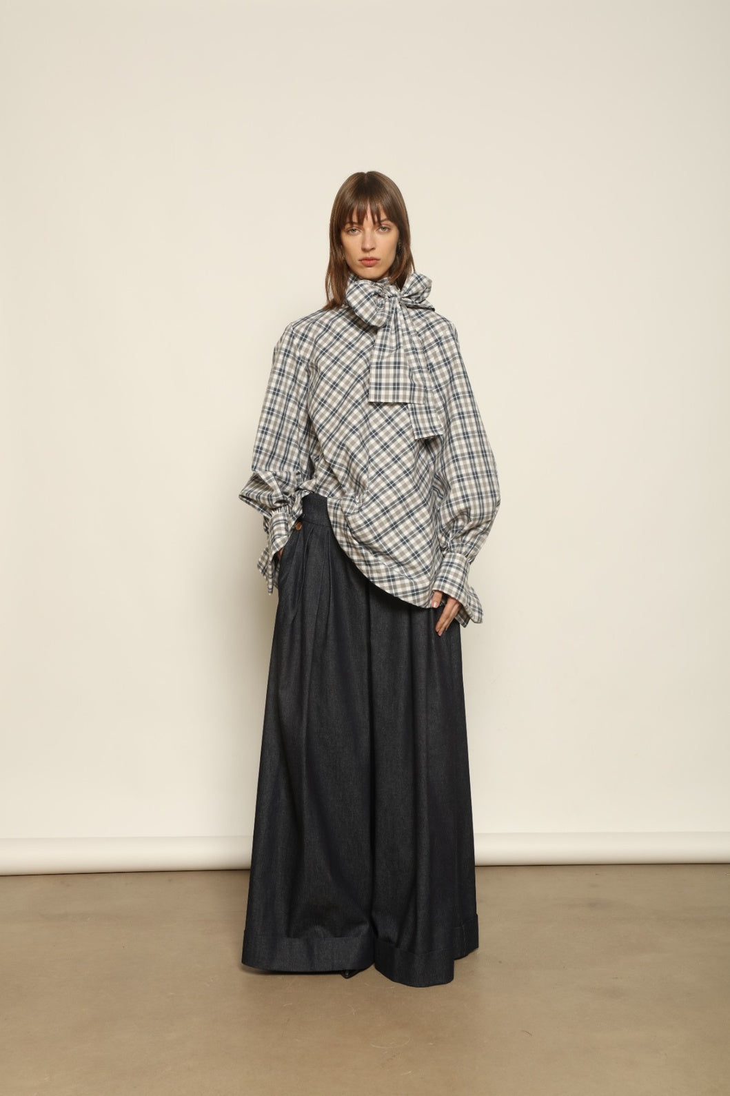 Model is wearing the Regula Maxi Check Popeline Cotton Blouse by House of Nomad Stories, crafted from crisp poplin cotton in an oversized check pattern with a waist tie and buttoned cuffs.