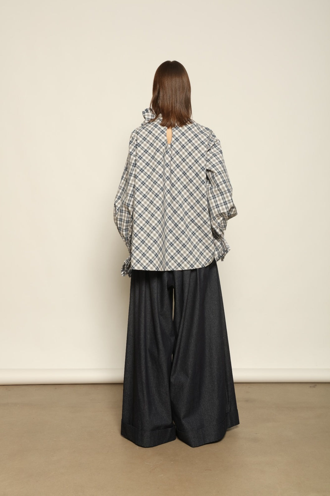 Model is wearing the Regula Maxi Check Popeline Cotton Blouse by House of Nomad Stories, crafted from crisp poplin cotton in an oversized check pattern with a waist tie and buttoned cuffs.