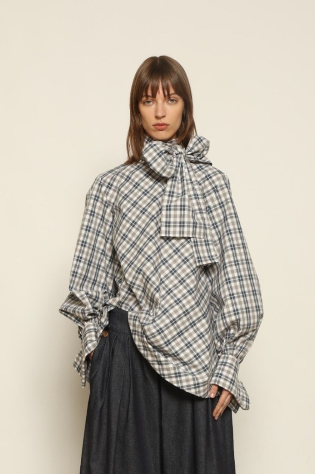 Model is wearing the Regula Maxi Check Popeline Cotton Blouse by House of Nomad Stories, crafted from crisp poplin cotton in an oversized check pattern with a waist tie and buttoned cuffs.