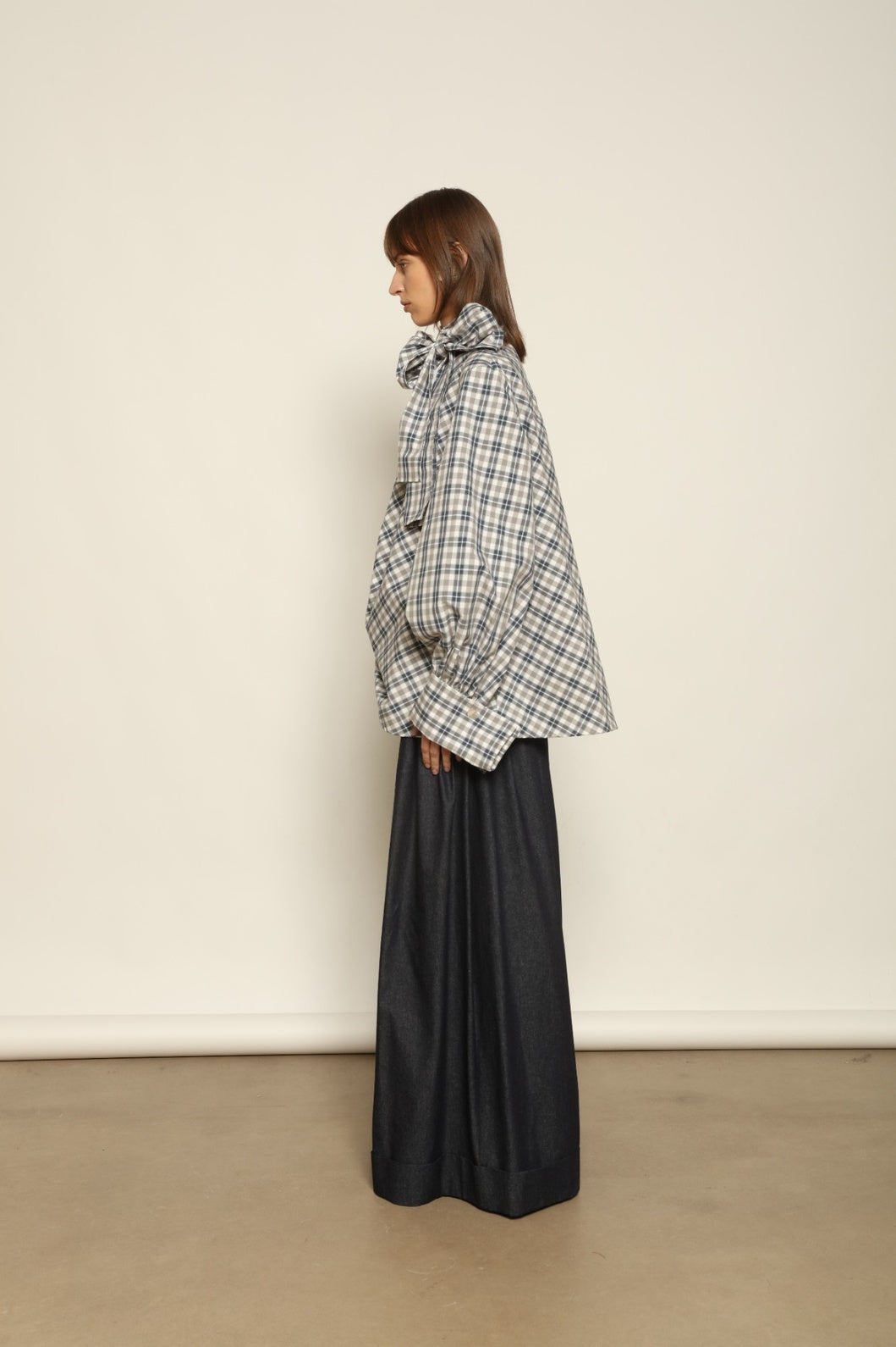 Model is wearing the Regula Maxi Check Popeline Cotton Blouse by House of Nomad Stories, crafted from crisp poplin cotton in an oversized check pattern with a waist tie and buttoned cuffs.
