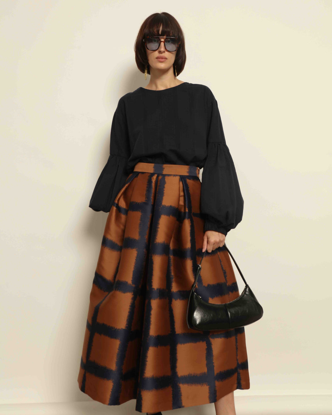 Model is wearing the Square Orange and Blue Skirt by Lunatica Milano. Pleated skirt in bronze and deep blue with striking geometric design. Feminine, elegant, and handcrafted in Italy. Part of House of Nomad Stories selection.