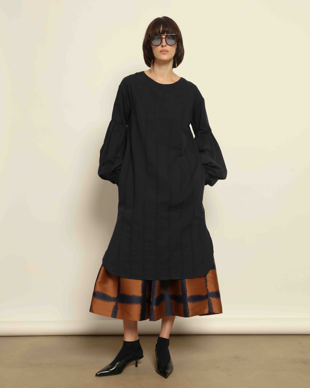Model is wearing the Square Orange and Blue Skirt by Lunatica Milano. Pleated skirt in bronze and deep blue with striking geometric design. Feminine, elegant, and handcrafted in Italy. Part of House of Woven Stories selection.