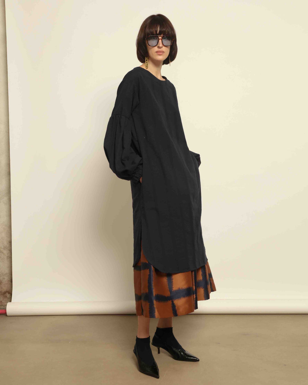 Model is wearing the Square Orange and Blue Skirt by Lunatica Milano. Pleated skirt in bronze and deep blue with striking geometric design. Feminine, elegant, and handcrafted in Italy. Part of House of Woven Stories selection.