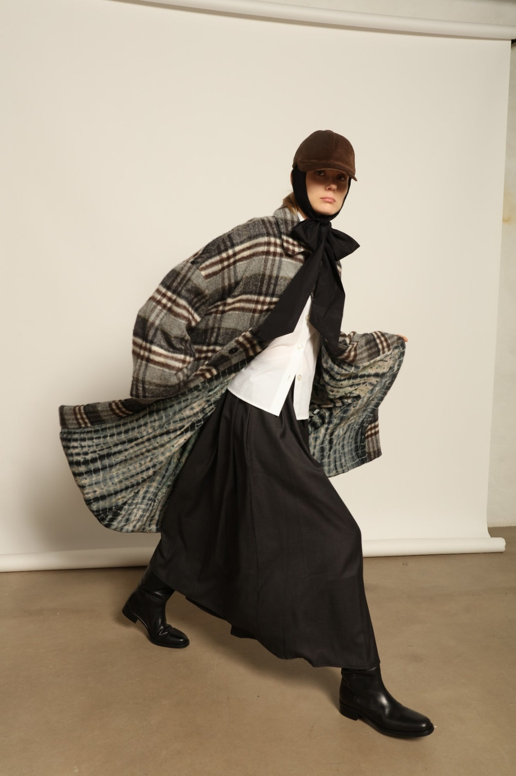 Model is wearing the Tiflis Checked Coat by House of Woven Stories, crafted from a soft wool blend with muted grey and brown checks, featuring an oversized silhouette, wide sleeves, and structured collar for timeless elegance.