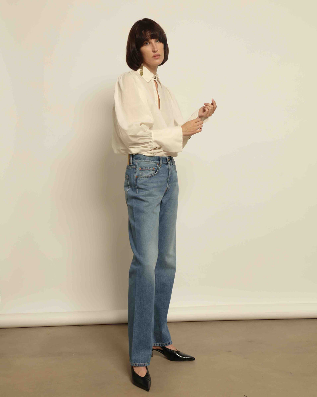 Model is wearing the Tilda Mid-Rise Draped Straight Jean by B Sides in classic indigo denim, mid-rise fit with straight tapered leg and curved inseam for a leg-lengthening silhouette.