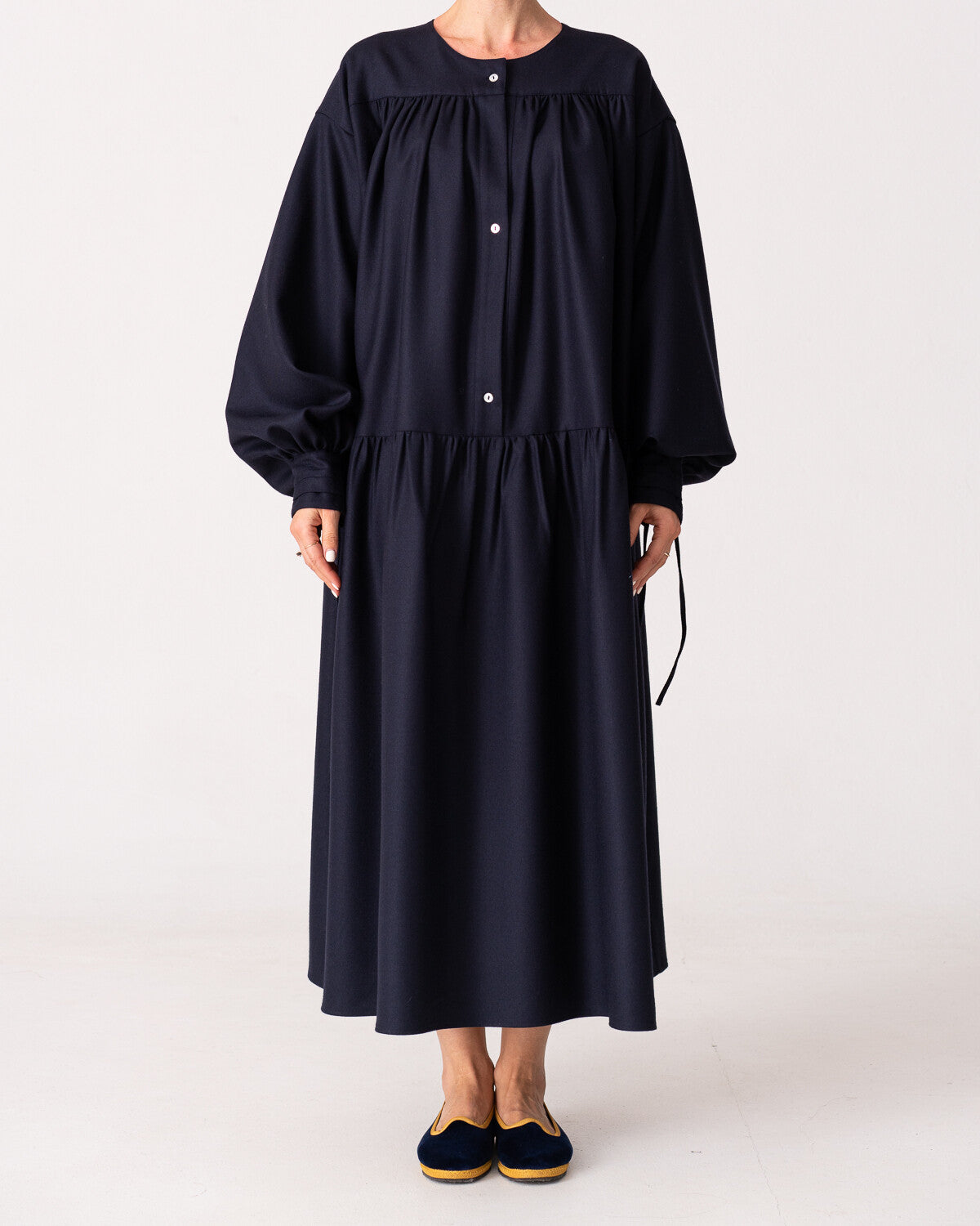 Model is wearing the Winter Calla Dress by Les Vacances d’Irina, a full-length navy merino wool dress with drop-waist silhouette, billowy sleeves, and bow cuffs, handmade in Bucharest and available at House of Nomad Stories.