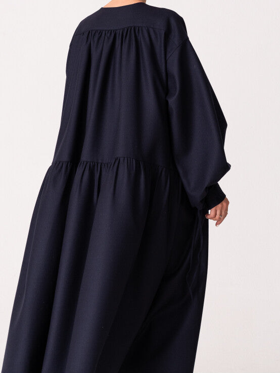 Model is wearing the Winter Calla Dress by Les Vacances d’Irina, a full-length navy merino wool dress with drop-waist silhouette, billowy sleeves, and bow cuffs, handmade in Bucharest and available at House of Nomad Stories.