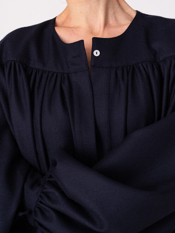 Model is wearing the Winter Calla Dress by Les Vacances d’Irina, a full-length navy merino wool dress with drop-waist silhouette, billowy sleeves, and bow cuffs, handmade in Bucharest and available at House of Nomad Stories.